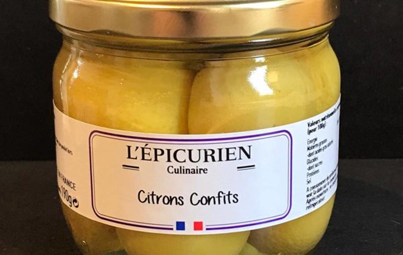 Un bocal en verre de citrons confits portant une étiquette blanche L’Épicurien Culinaire, sur un fond sombre.