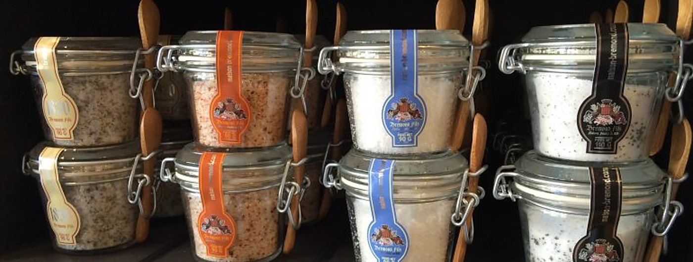 Des bocaux de sels aromatisés avec leurs cuillères en bois, alignés sur une étagère.