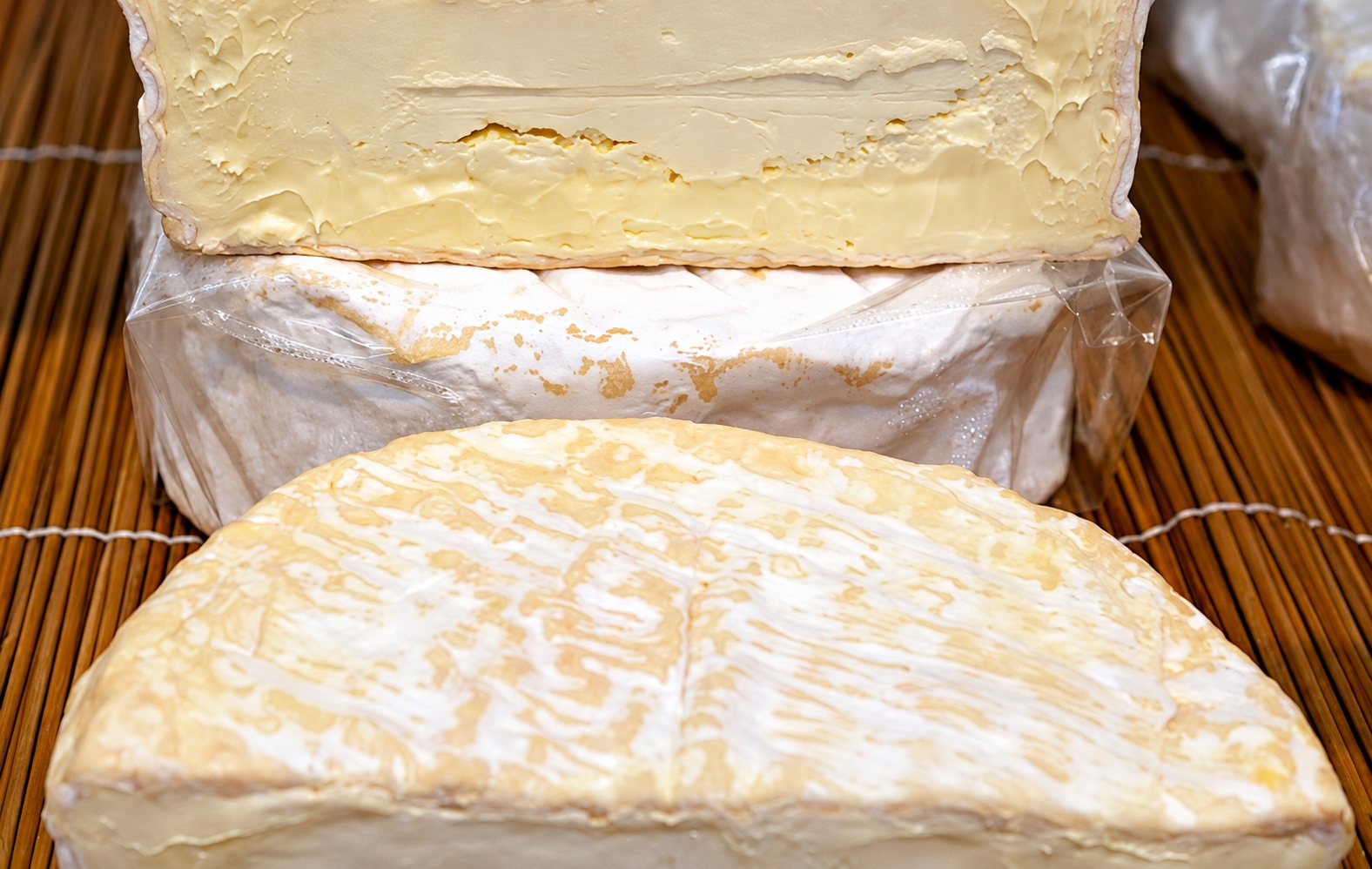 Des fromages à croûte fleurie, entiers et coupés, sur une natte en bambou.