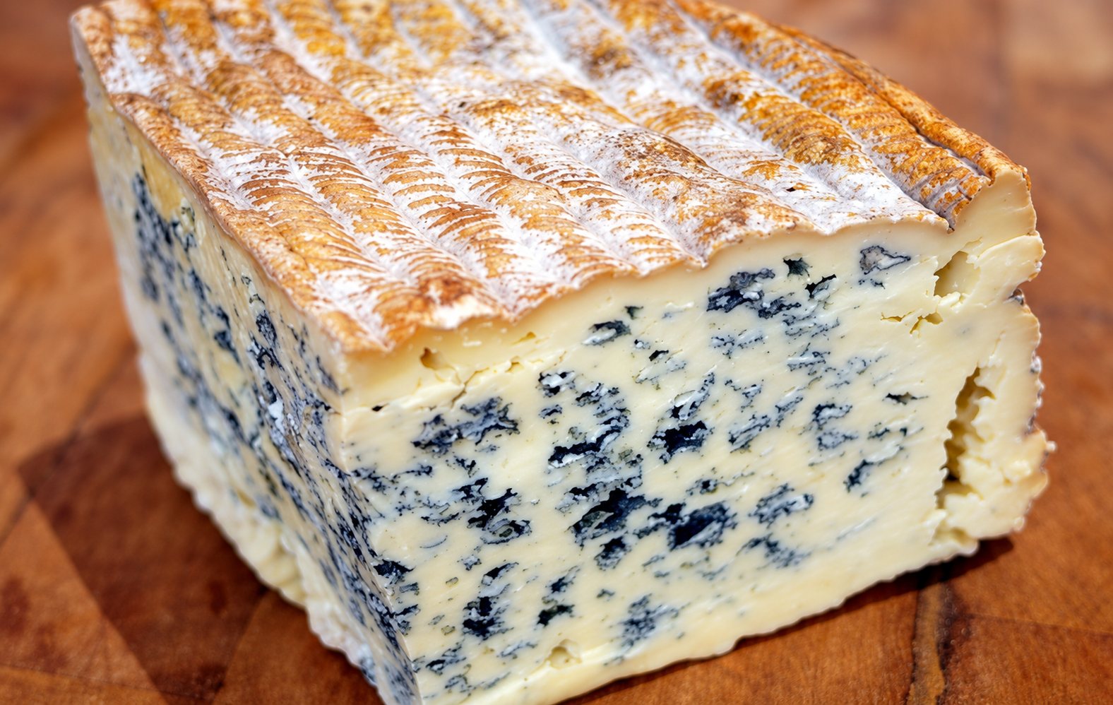 Gros plan sur un morceau de fromage bleu à la pâte marbrée de veines bleu-vert, posé sur une planche en bois.